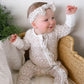 Baby in a floral pajamas outfit sitting on a wicker chair with a white background