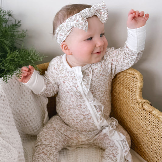 Baby in a floral pajamas outfit sitting on a wicker chair with a white background